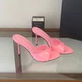 Close-up of vibrant pink patent leather stiletto mules on a reflective glass table - Pink