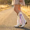 Close-up of white cowboy boots decorated with a purple ribbon bow and pearl charm. - Purple