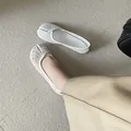 Detailed macro view of white mesh split-toe tabi flat shoes worn with beige trousers - 35 / White