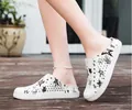 Detail view of white perforated clogs featuring black star patterns on wooden outdoor deck. - Star