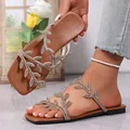 Close-up detail of brown flat sandals featuring sparkling rhinestone leaf straps. - Brown