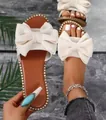 Detail of cream bow slide sandal with rhinestone trim shown on foot and held by hand. - 36 / Beige