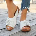 Close-up detail of white women's wedge sandals with floral decoration on a wooden deck - White