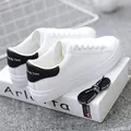 Close-up of white sneakers with black heel accent and decorative laces on a book. - 35 / Black and White Color Block Style / Black