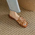 Close-up detail shot of elegant brown woven flat sandals worn on a rustic woven rug mat - 35 / Dark Brown