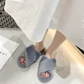 Detalle de pantuflas de felpa gris con tiras cruzadas en los pies de una modelo en casa - Gris