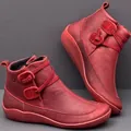 Macro view of textured red leather ankle boots featuring unique button strap design and flat soles - 35 / Red