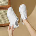 Detailed shot of stylish white athletic sneakers held against a soft beige backdrop - 35 / White