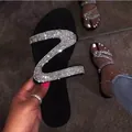 Detail view of black flat sandals with a sparkling Z-shaped rhinestone strap design. - 36 / Silver
