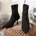 Close-up of black pointed-toe knit stiletto ankle boots displayed on a woven surface - 36 / Black