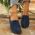 Close-up view of navy blue suede clogs featuring white stitching on stone floor. - 36 / Navy Blue