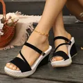 Close-up view of black wedge sandals with textured straw platforms on wooden steps. - 36 / Black