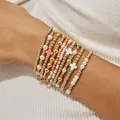 Close-up van een set stapelbare elastische kralenarmbanden met gouden kralen en parels - Kruis & Gekleurde Rijstkralen Armband Set (JZ-ZZ-019-19)