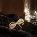 Elegant gold-toned bow brooch pin featuring sparkling crystal accents on dark velvet fabric - Full Rhinestone Bow Style (BH26)
