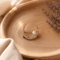 Dettaglio di una spilla a mezzaluna con diamanti scintillanti e una perla bianca - Oro