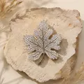 Gedetailleerde weergave van een fonkelende zilverkleurige esdoornbladbroche op natuursteen. - Zilveren esdoornblad broche