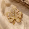 Gedetailleerd beeld van een elegante esdoornbladbroche met gouden kristallen op linnen. - Gouden Esdoornblad Broche