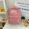 Detailweergave van de rood-wit geruite schoolrugzak met witte strik op een witte tafel. - Rood