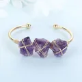 Close-up detail of three purple raw amethyst stones wire-wrapped on a gold open bangle - Purple Crystal