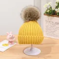 Detail der gelben Kinder-Strickmütze mit weichem Kunstfell-Bommel-Dekor - Kurkuma