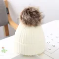 Nahaufnahme einer weißen Strickmütze für Babys mit einem großen flauschigen braunen Bommel - Weiß