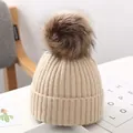 Nahaufnahme einer warmen beigen Strickmütze mit flauschigem Kunstfellbommel für Kinder. - Gebrochenes Weiß