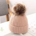Detailansicht einer rosa gestrickten Babymütze mit flauschigem braunem Kunstfellbommel - Hellrosa