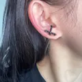 Close-up detail of a black sword-shaped dagger earring worn on an Asian model's ear - Cross Sword Stud Earrings (1 Pair) / Black Zirconia