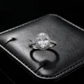Gros plan d'une bague classique en moissanite à coupe ovale avec halo sur son écrin noir. - Bague (T16) / Blanc