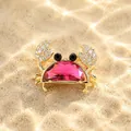 Detailed macro view of a gold-toned crab brooch with a vibrant pink crystal body on sand - Wine Red Crystal Crab Brooch / Burgundy