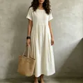 Lifestyle view of white pleated cotton linen dress with woven bag accessory - S / Dresses / White