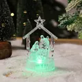 Close-up of a clear crystal Nativity scene figurine with glowing green LED light on snow - Style 2