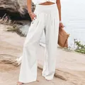 Women's high-waisted white linen wide-leg trousers shown in a stylish beach setting. - White