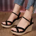 Close-up of black platform wedge sandals with ankle strap and woven sole on a model's feet. - 35 / Black