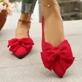 Close-up of red pointed-toe flat sandals featuring a large decorative fabric bow. - 36 / Red