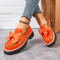 Detail view of orange patent leather loafers with large bow and thick lug sole. - Orange Red