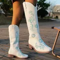 Detailed view of white knee-high boots with blue floral embroidery and square heel. - 36 / White