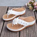 Nahaufnahme von weißen Keilsandalen mit einer dekorativen Blume und Metallnieten - 36 / Weiß