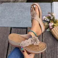 Gedetailleerd overzicht van teenslippers met sleehak, bloemen en klinknagels op hout. - Beige