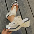 Detailansicht cremefarbener Keilsandaletten mit Strohstruktur und Goldnieten auf Holzdeck. - 36 / Beige