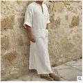 A man wearing a long, loose-fit white cotton linen robe standing against a stone wall. - 3XL / Robe / Square Pocket Style / Off White