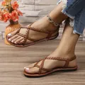 Detail view of brown braided strappy flat sandals with toe-clip design on a model's feet. - 36 / Tan