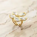 Detalle macro de un elegante anillo de flores chapado en oro con pétalos blancos en mármol - Abierto Ajustable / Anillo de Flor con Textura de Concha Blanco Perla / Blanco Roto