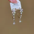 Detail van zilveren creolen met fonkelende zirkoon vlinder en druppelvormige kwastje - Stalen pin stijl / Zilver