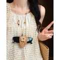 Bohemian bloem zonnebrilhouder ketting detail op model met een crème-gekleurd gehaakt vest - Bloemstijl / Ketting-Koffie