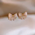 Nahaufnahme eleganter goldener Schleifenohrringe mit Kristallen und weißen Perlen - Schleife Stil (HE22516) / Gold