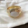 Dettaglio di un bracciale a polsino dorato con un intarsio ovale in resina bianca - Vestibilità ampia / Oro-Bianco