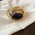 Primo piano di un lussuoso bracciale rigido dorato con resina ovale marrone scuro - Vestibilità ampia / Marrone oro