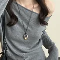 Detail eines ovalen Metallanhängers an einer schwarzen Lederschnur über grauem Pullover - Glänzender Stil / Silber