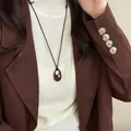 Close-up view of a stylish minimalist brown oval pendant necklace on a black cord - Black-Red